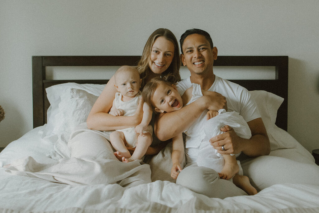 family snuggled up on a bed and smiling during a in-home family photo session 